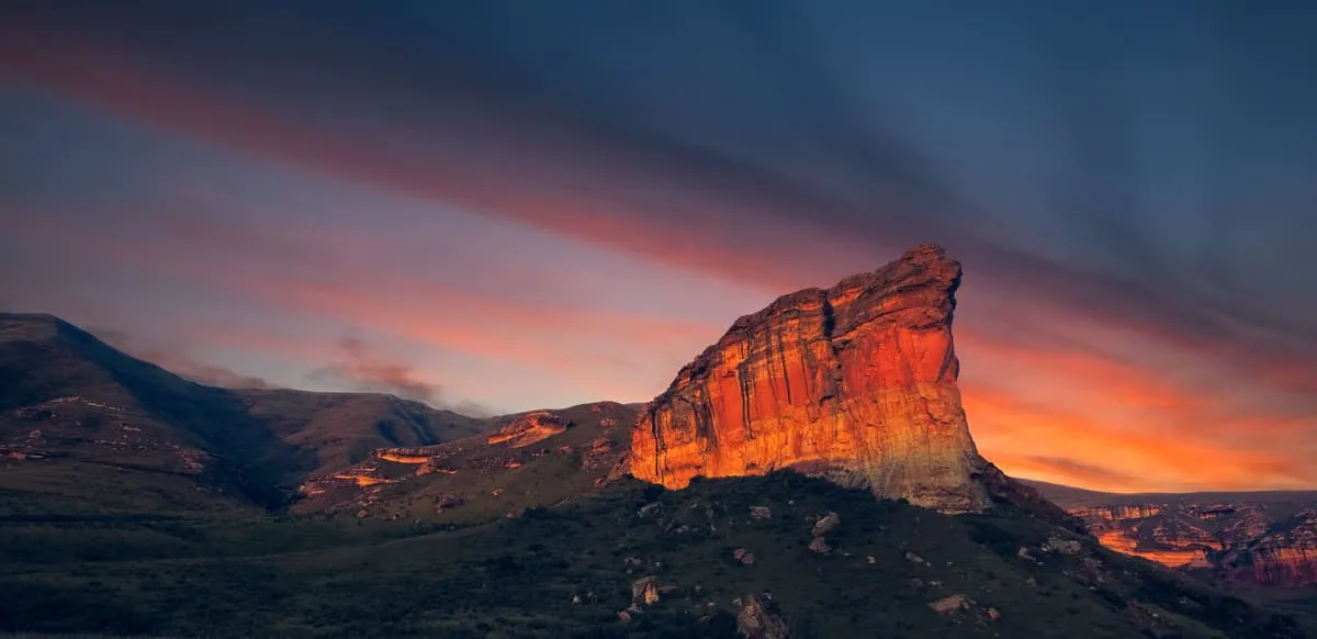 Spektakulärer Sonnenuntergang über einer erleuchteten Felsformation in einer malerischen Berglandschaft.