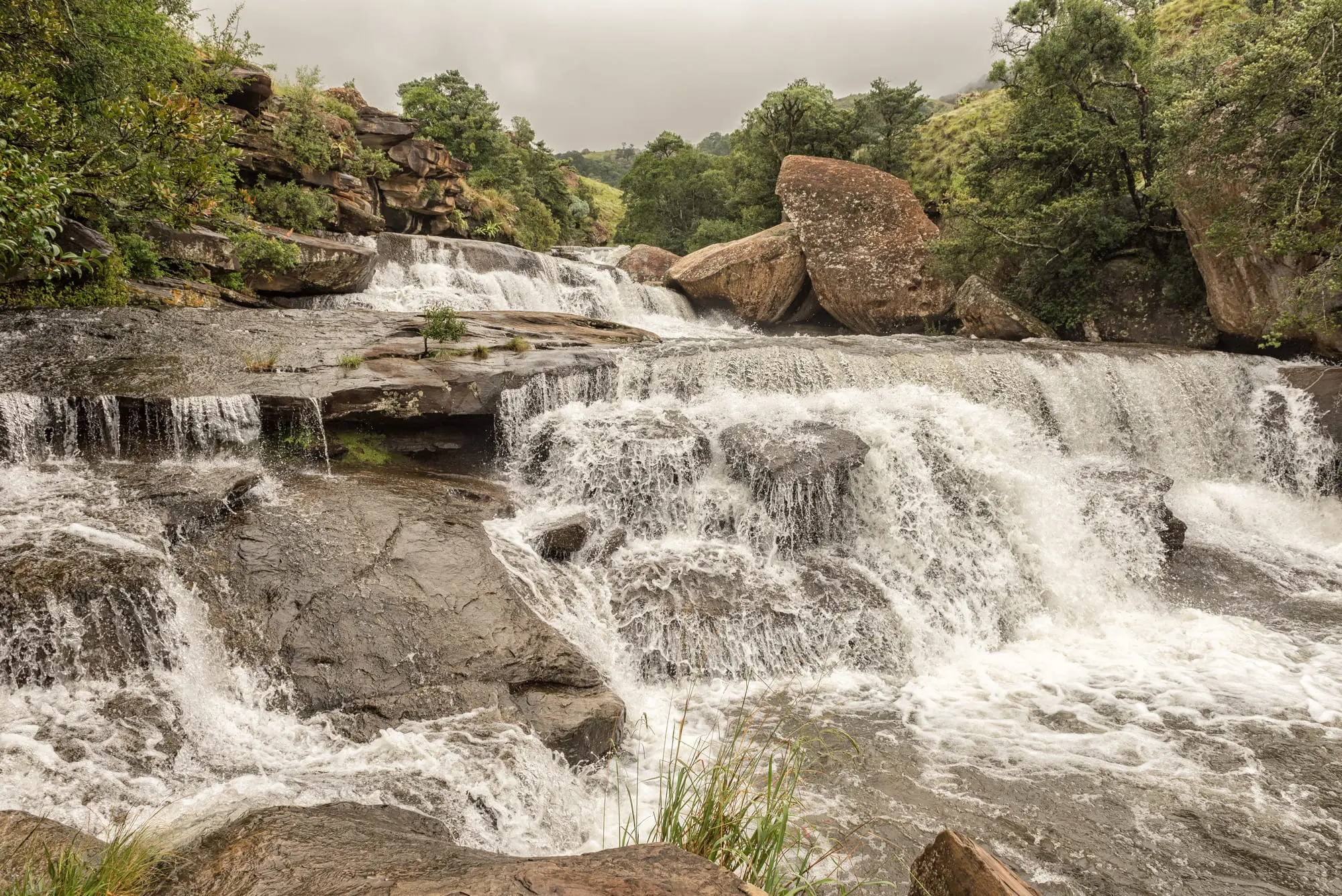 Kaskadierender Wasserfall inmitten grüner Natur, umgeben von Felsen und üppigem Wald.