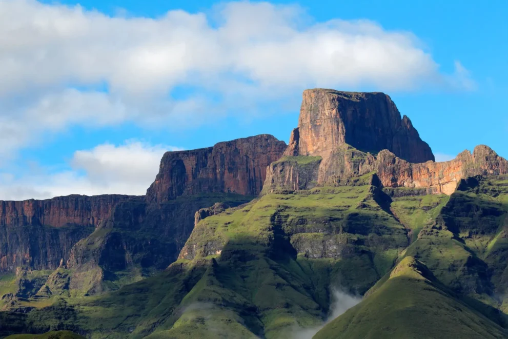 Majestätische Berglandschaft mit steilen Klippen, üppigem Grün und klarem Himmel.