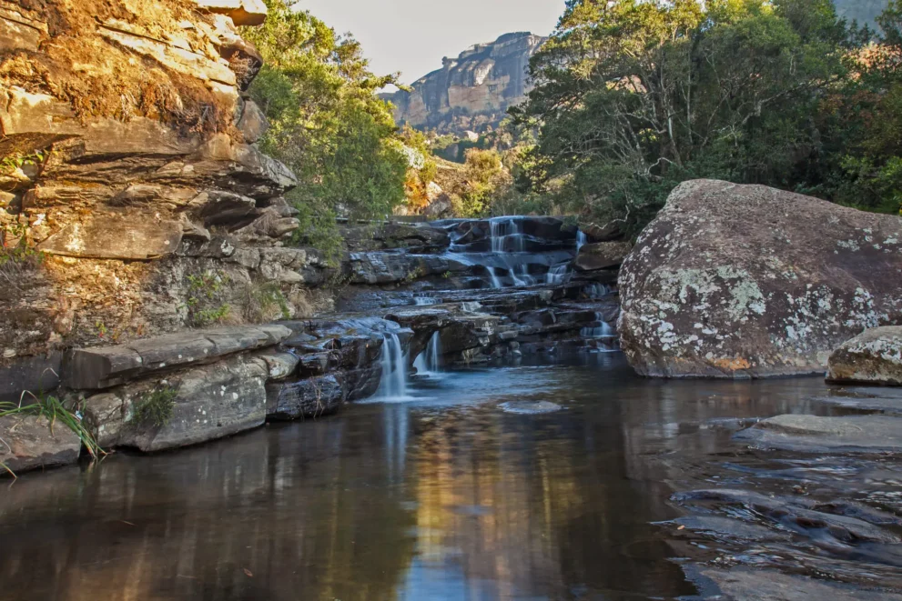 Kaskadierende Wasserfälle in ruhiger Naturkulisse, umgeben von Felsen und üppigem Grün unter strahlendem Himmel.