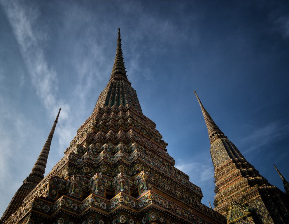 Mit Porzellan verzierte Chedis im Tempel Wat Pho in der Altstadt Rattanakosin von Bangkok vor blauem Himmel