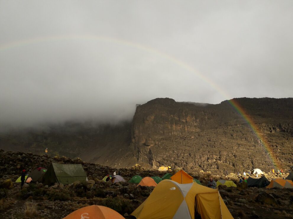 Regenbogen über der Great Barranco Wall, darunter die Zelte des Barranco Camps am Kilimandscharo