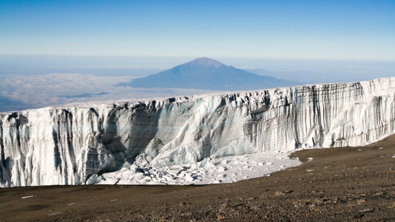 Gletscherwand nahe dem Uhuru Peak am Kilimandscharo, im Hintergrund der Mount Meru über den Wolken