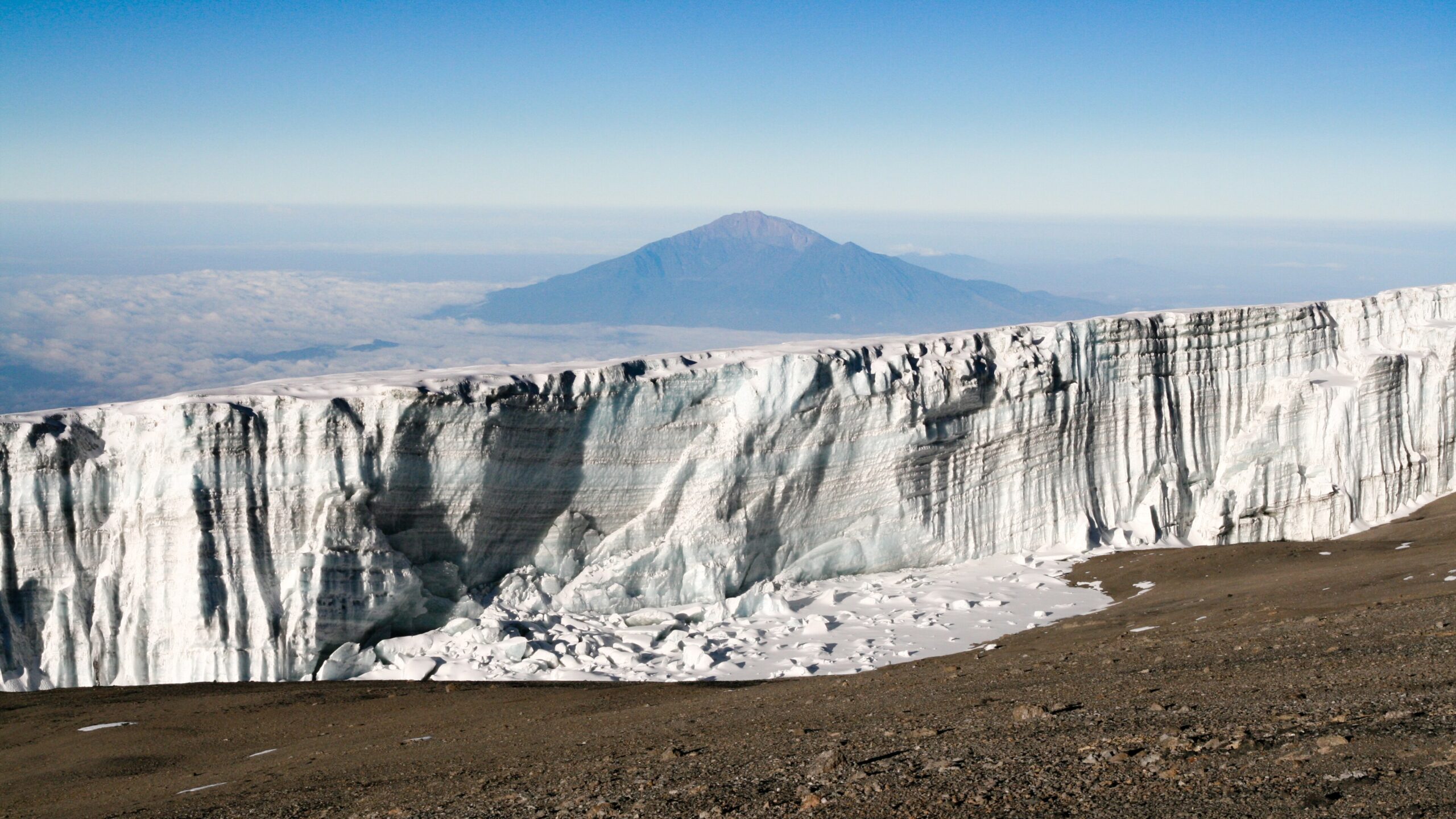 Gletscherwand nahe dem Uhuru Peak am Kilimandscharo, im Hintergrund der Mount Meru über den Wolken