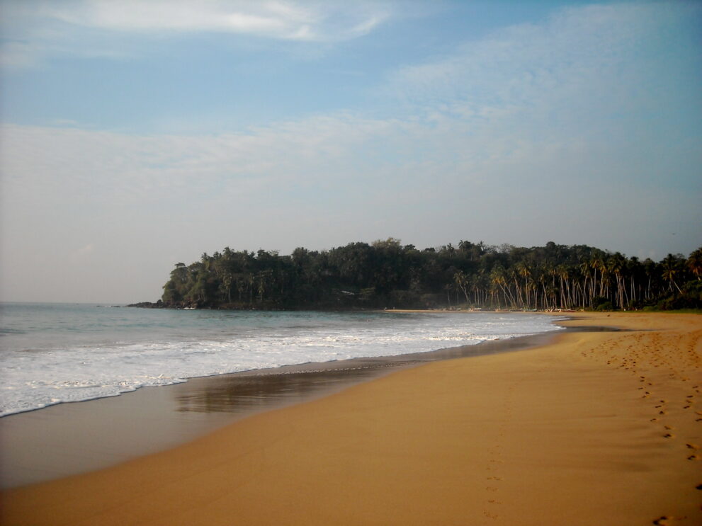 Der leere Sandstrand von Talalla an der Südküste Sri Lankas mit bewaldeter Landzunge am Ende der Bucht