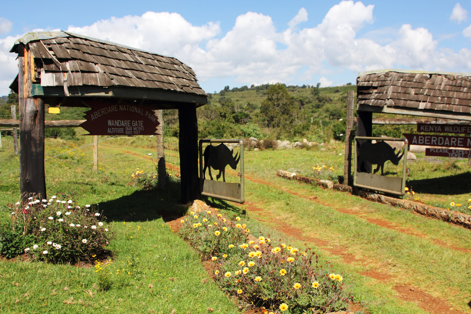 Das Wandare-Tor des Aberdare-Nationalparks mit Schindeldächern, Gattern mit Nashorn-Silhouette und Blumenbeeten