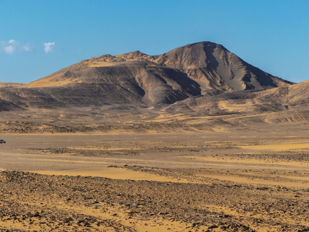 Dunkle Hügel und schwarze Dünen von Adjalati über einer Kiesebene im Roten Tadrart, Algerien