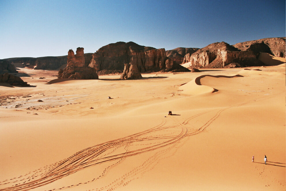 Fahrspuren von Geländewagen im Sand vor den Felsformationen von Bouhediane im Roten Tadrart