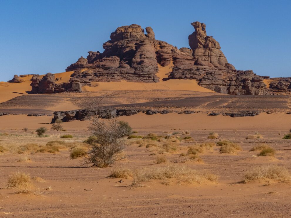 Zerklüftete Sandsteinformation von El Berdj über Sand und Akazien im Roten Tadrart, Algerien