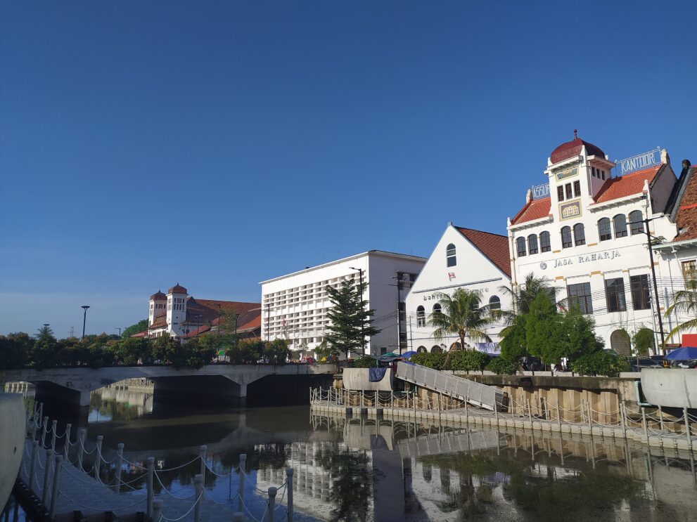 Koloniale Gebäude der Altstadt Kota Tua in Jakarta spiegeln sich im Kanal Kali Besar unter blauem Himmel