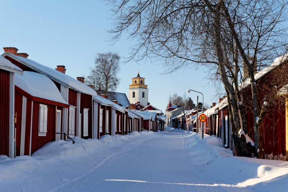 Rote Kirchhäuser in der Kirchstadt Gammelstad bei Luleå im Schnee, hinten der Glockenturm
