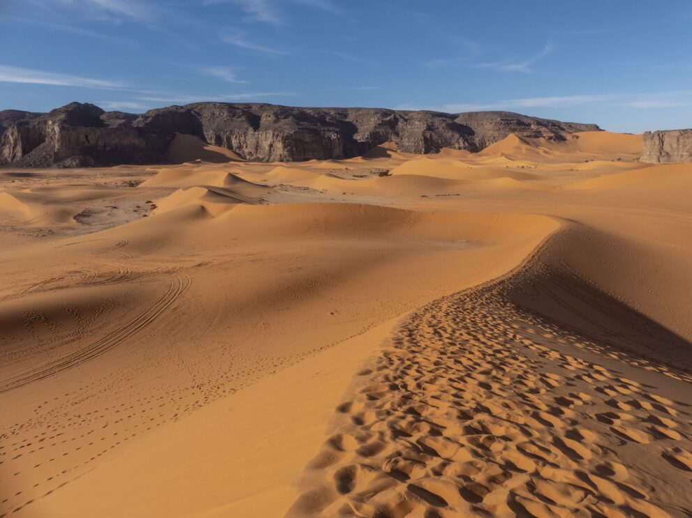 Dünenkamm mit Fußspuren vor den Felswänden von Moul N'Aga im Roten Tadrart, Südosten Algeriens