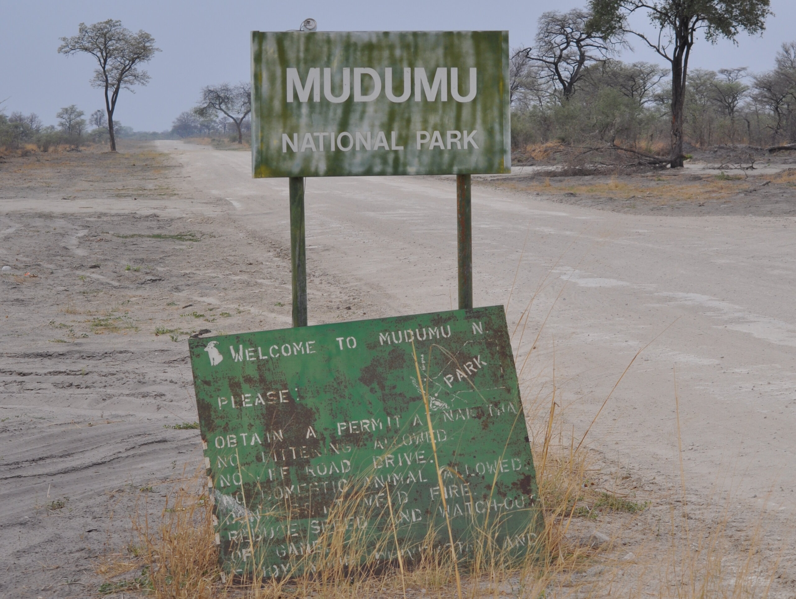 Grünes Schild Mudumu National Park an einer hellen Sandpiste zwischen lichten Bäumen