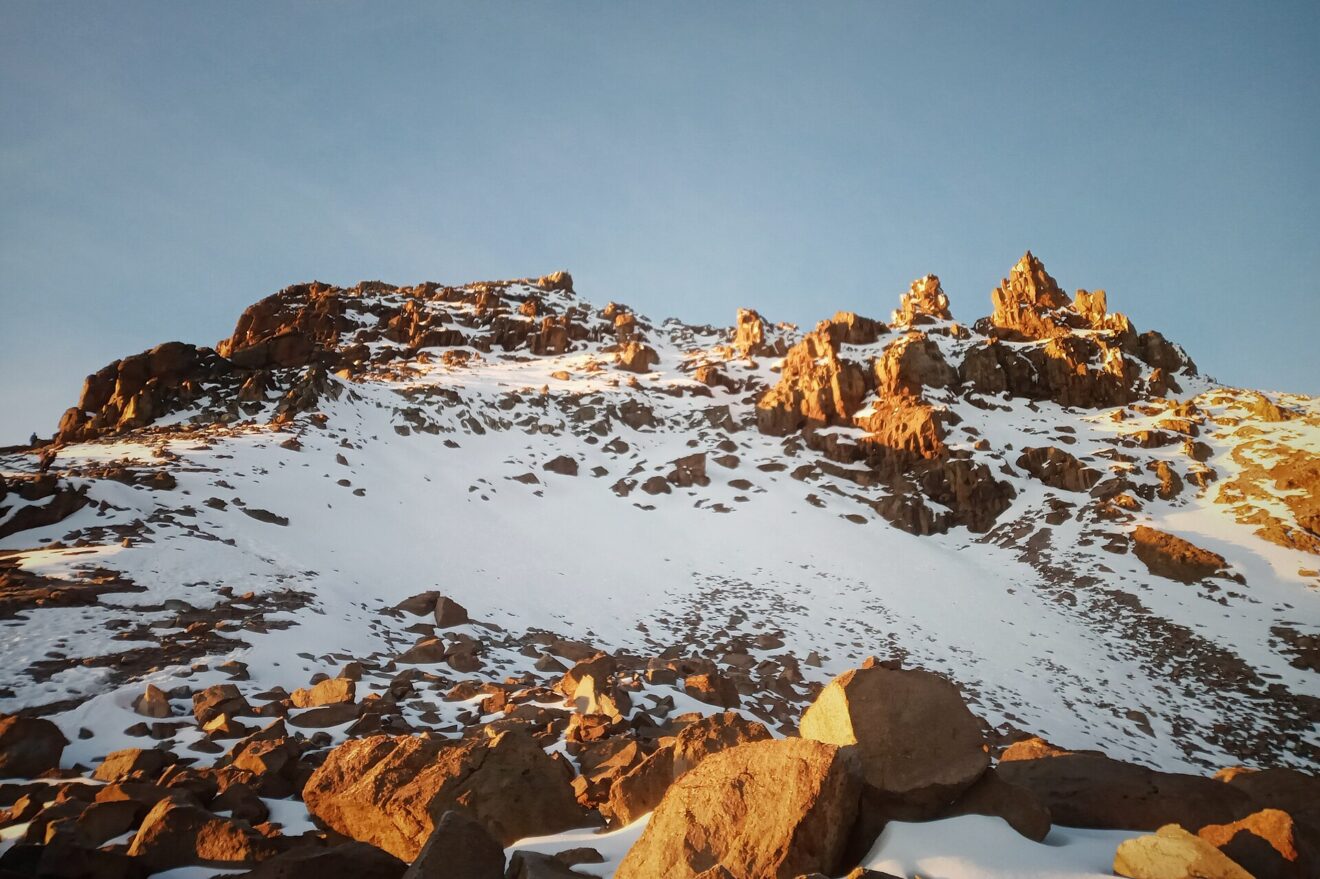 Felszacken und Schneehang kurz unter dem Gipfel von Point Lenana, die Felsen leuchten orange im Morgenlicht