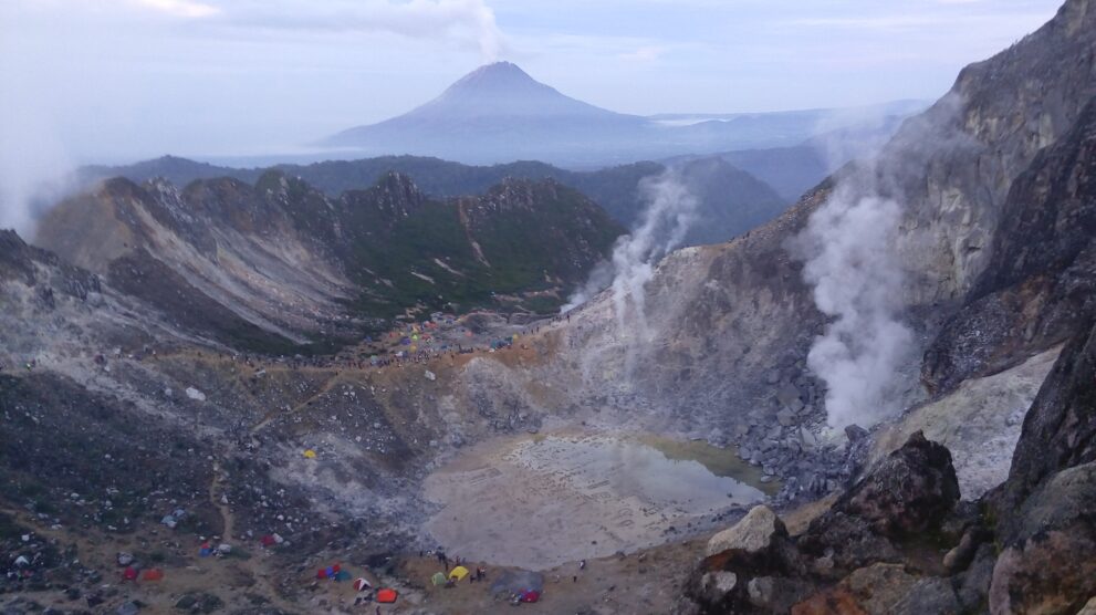 Krater des Vulkans Sibayak bei Berastagi auf Sumatra mit dampfenden Fumarolen, im Hintergrund der Kegel des Sinabung