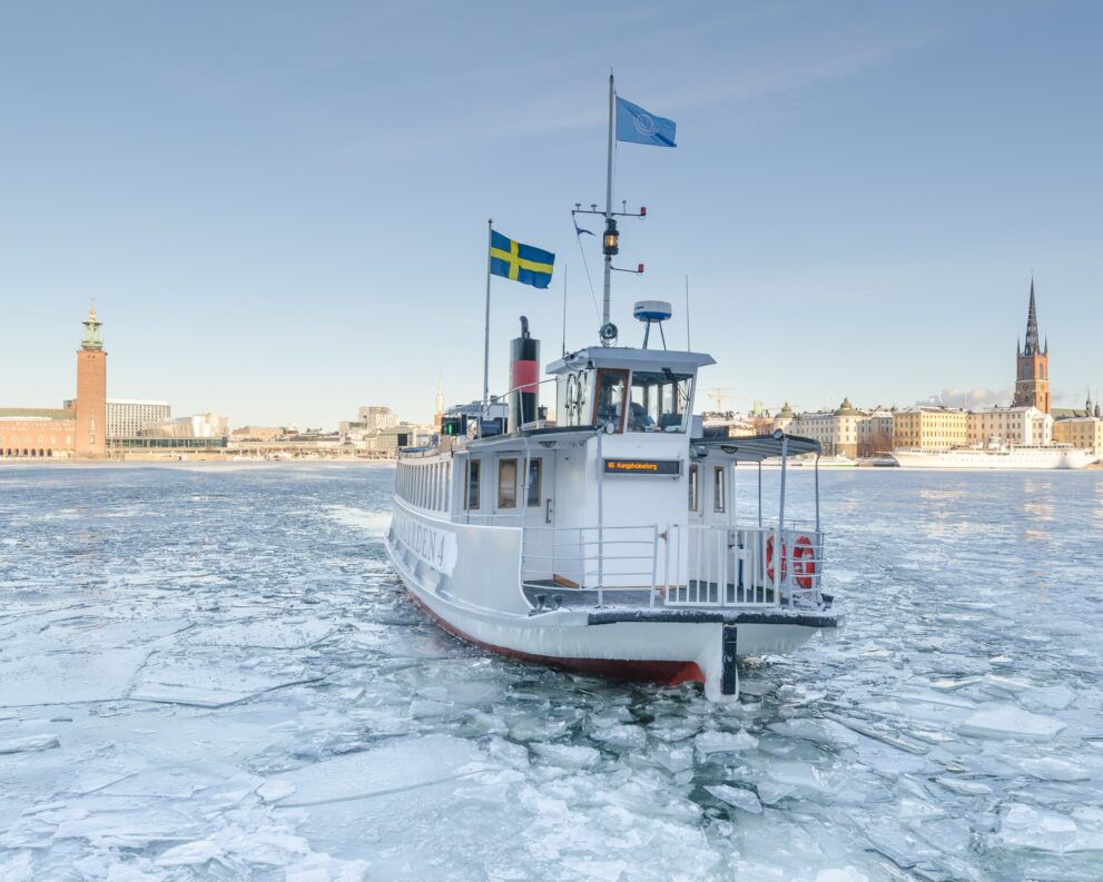 Fähre im Eis der Riddarfjärden in Stockholm, dahinter Stadshuset und Riddarholmskyrkan