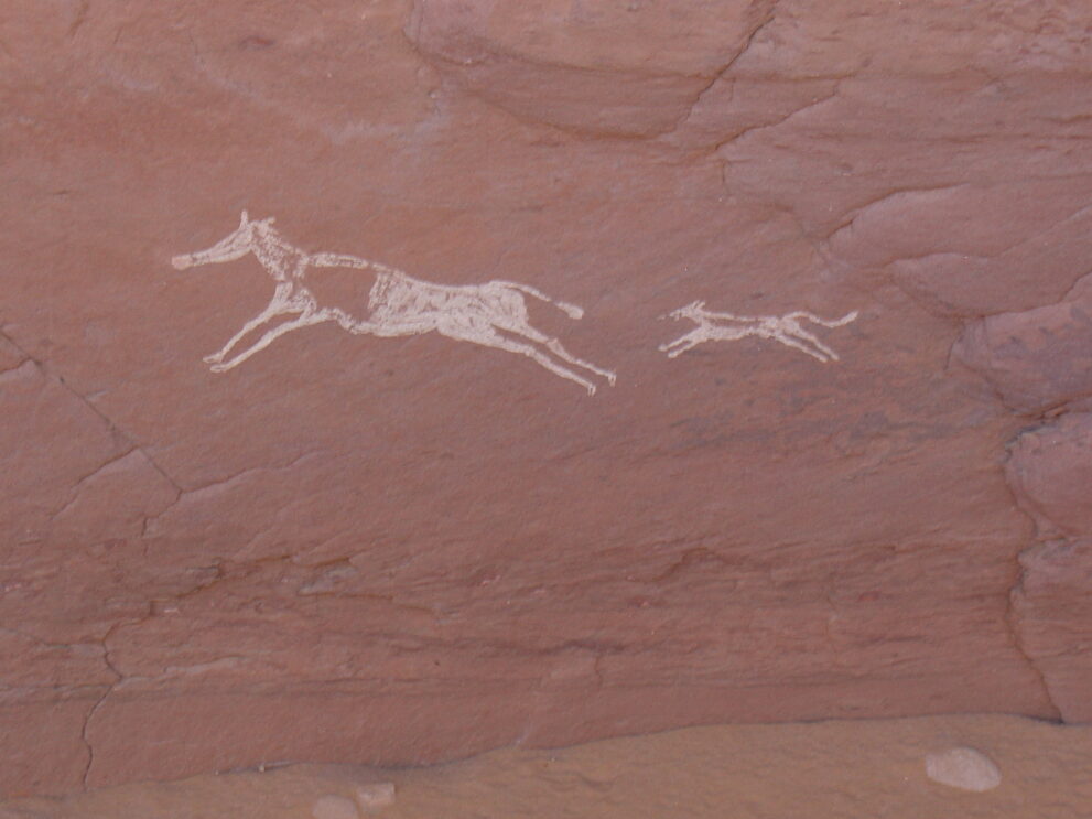 Helle Felszeichnung zweier laufender Tiere auf rötlichem Sandstein im Roten Tadrart in Algerien