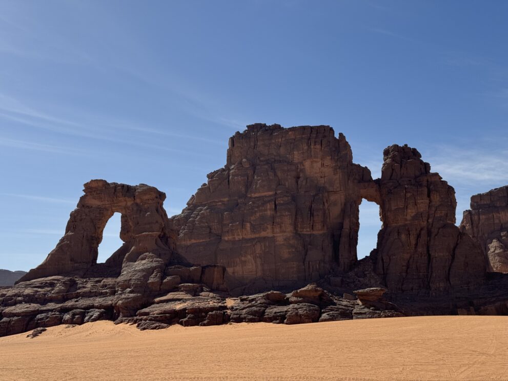 Sandsteinfelsen mit zwei natürlichen Felsbögen in einer Sandebene des Roten Tadrart in Algerien