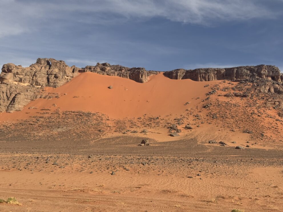 Rote Düne an einer Sandsteinwand über einer Kiesebene im Roten Tadrart im Südosten Algeriens