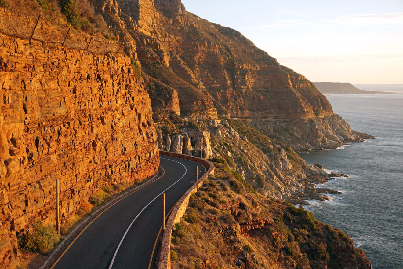 Die Küstenstraße Chapman's Peak Drive führt in der Abendsonne durch eine rote Felswand über dem Atlantik