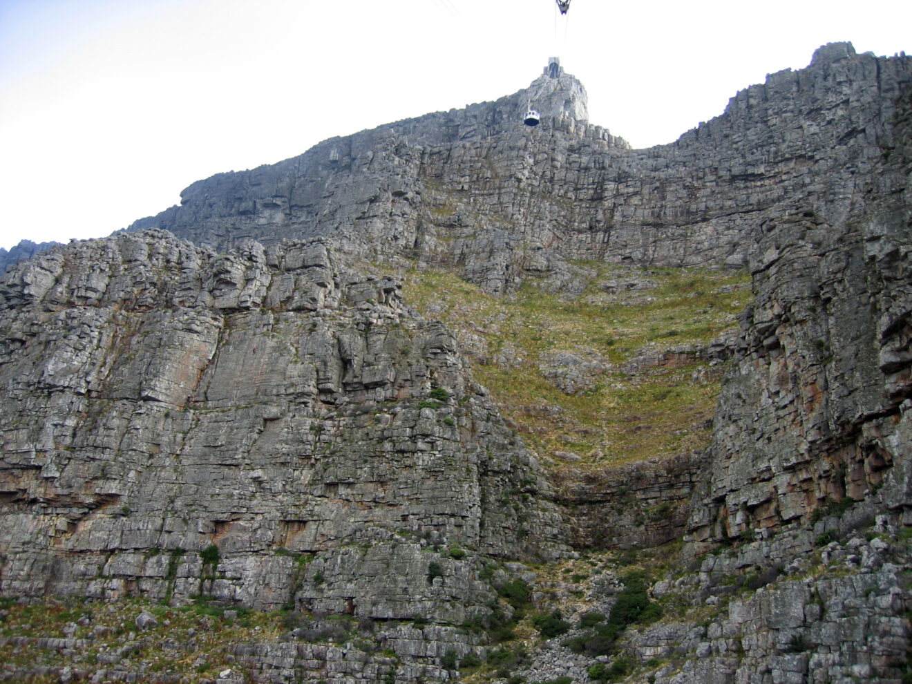 Die runde Gondel der Tafelberg-Seilbahn hängt kurz unter der Bergstation vor der grauen Felswand des Tafelbergs
