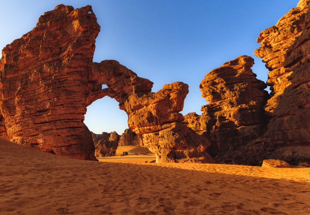 Felsbogen von Tikoubaouine im Tassili n Ajjer bei Djanet, rote Sandsteinwände über hellem Sand