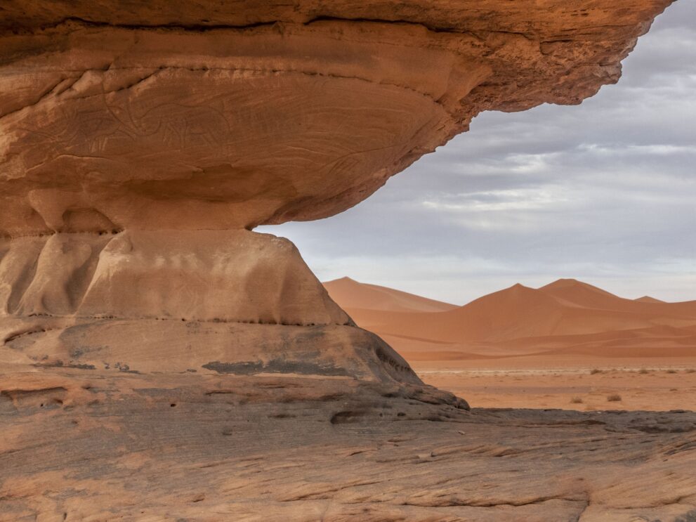 Felsdach mit Gravur eines Nashorns bei Tin Merzouga, dahinter die roten Dünen des Tadrart
