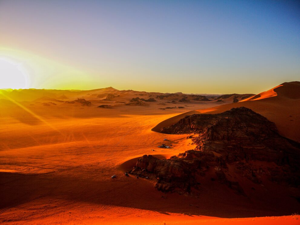 Sonnenuntergang vom Kamm der großen Düne von Tin Merzouga über Felsen und Sand im Roten Tadrart