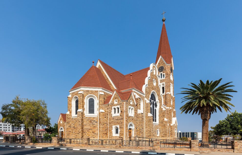 Christuskirche in Windhoek, evangelisch-lutherische Kirche aus Sandstein mit rotem Dach und Palme davor
