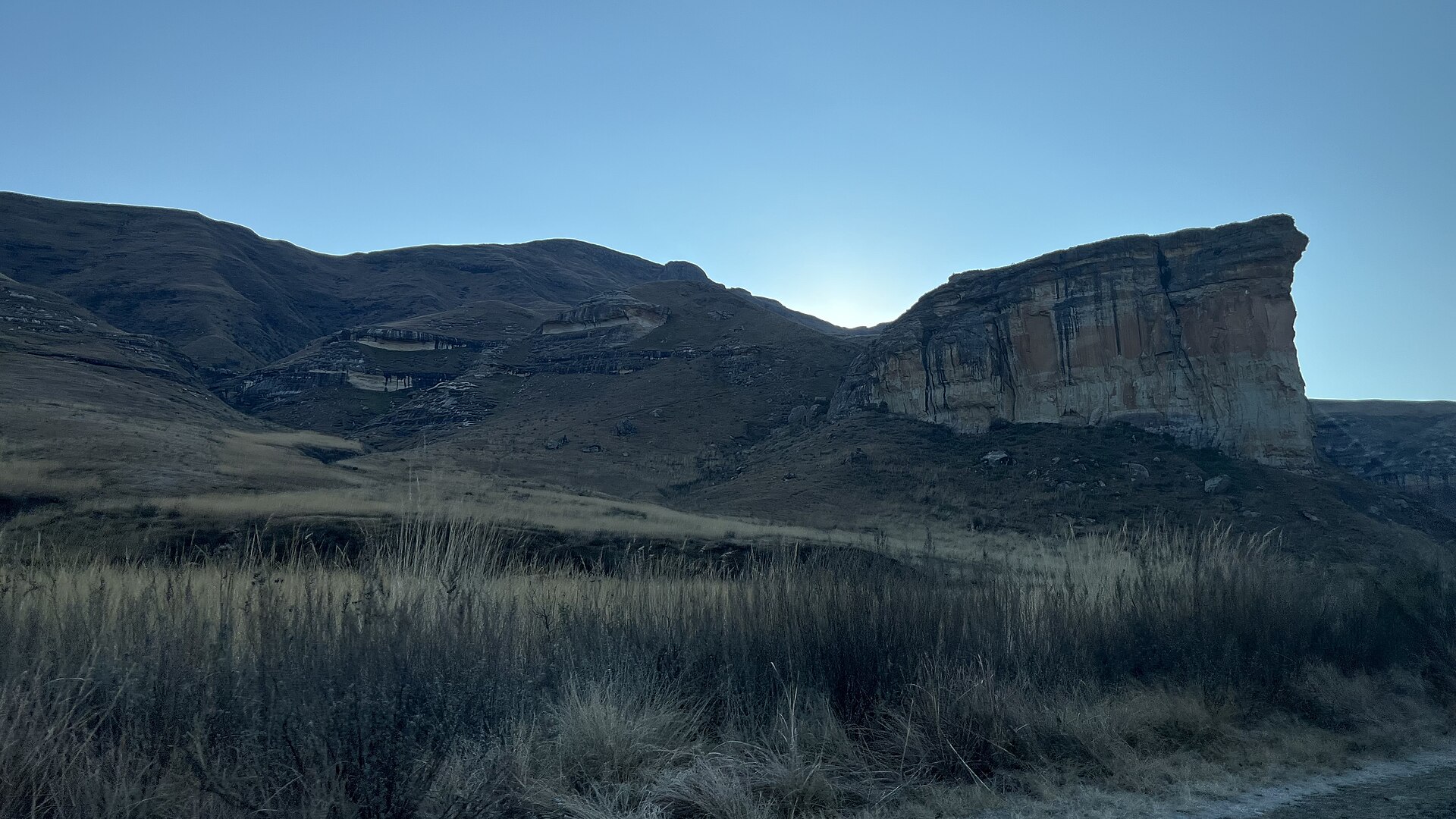 Der Brandwag-Felsen im Gegenlicht eines Wintermorgens, davor trockenes Gras