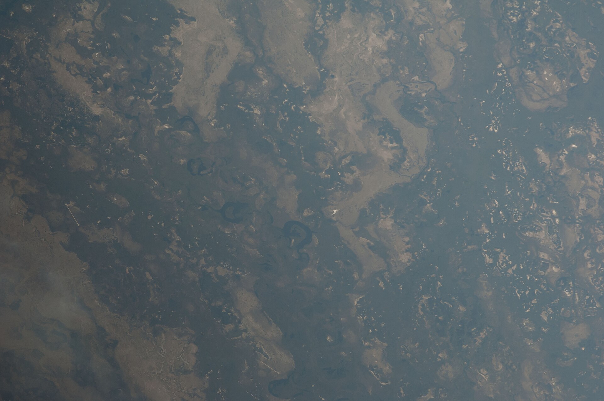 Schrägaufnahme aus dem All auf das Okavango-Delta: dunkle Wasserflächen, helle Inseln und mehrere runde, dunkle Lagunen in der Bildmitte.