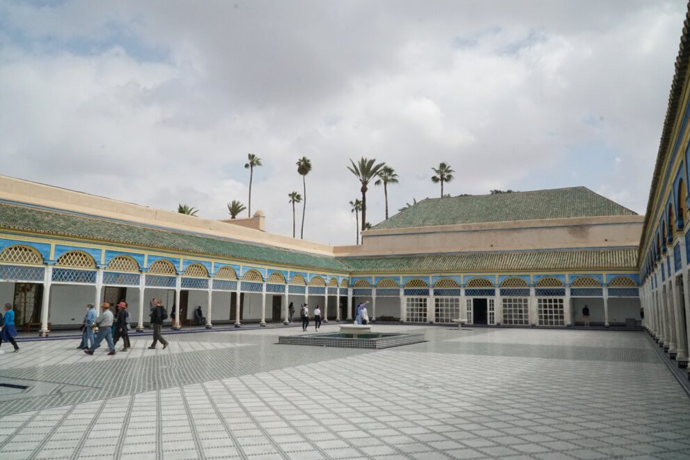 Großer Hof des Bahia-Palasts in Marrakesch mit Marmorboden, Brunnen und blau bemalten Arkaden unter Palmen