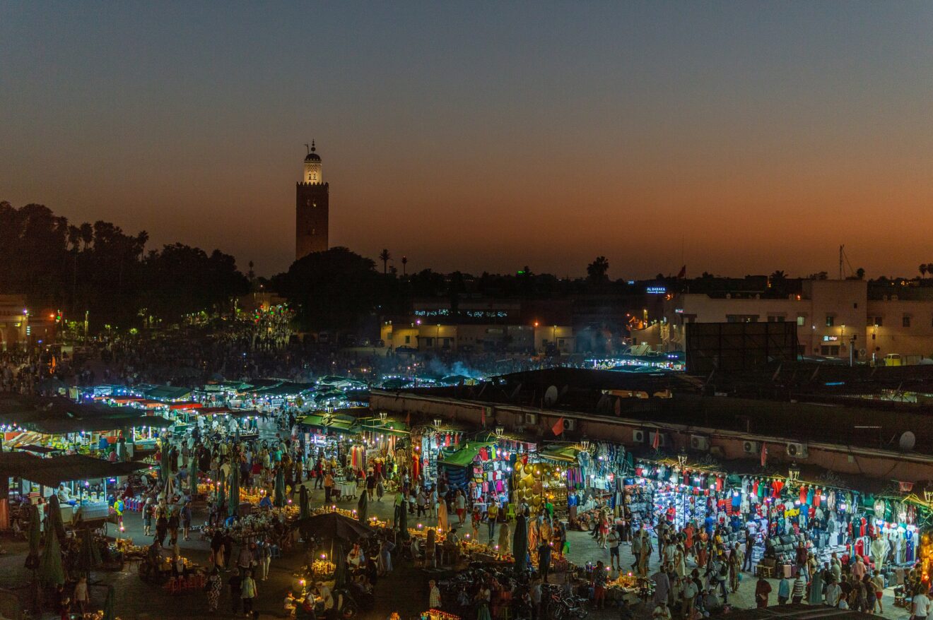 Jemaa el-Fna in der Abenddämmerung von oben, Garküchen leuchten, dahinter das Minarett der Koutoubia in Marrakesch