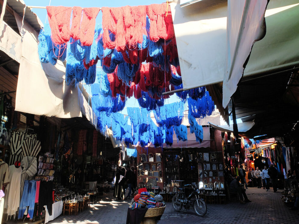 Gefärbte Wollstränge in Rot und Blau hängen über der Gasse im Souk der Färber in der Medina von Marrakesch