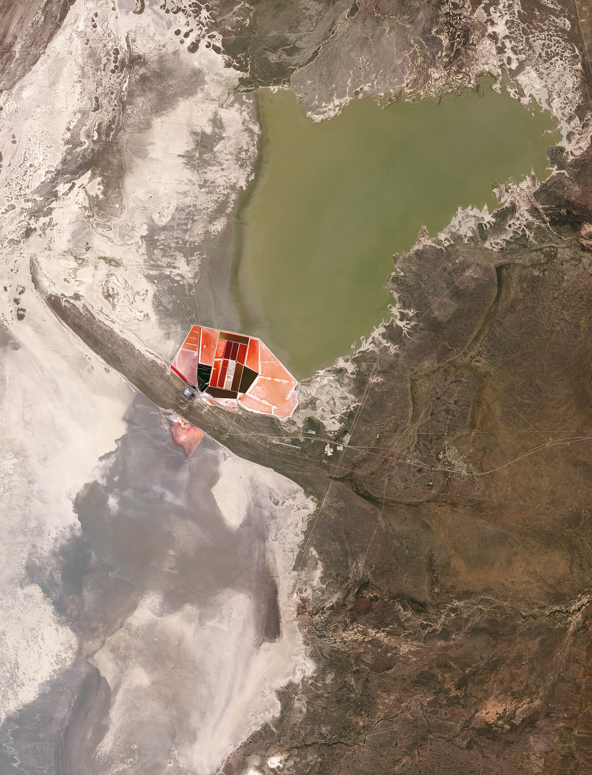 Satellitenbild: links weiße und graue Pfannenflächen, oben ein großer grünlicher Wassersee, in der Mitte rot und rosa gefärbte rechteckige Verdunstungsbecken.