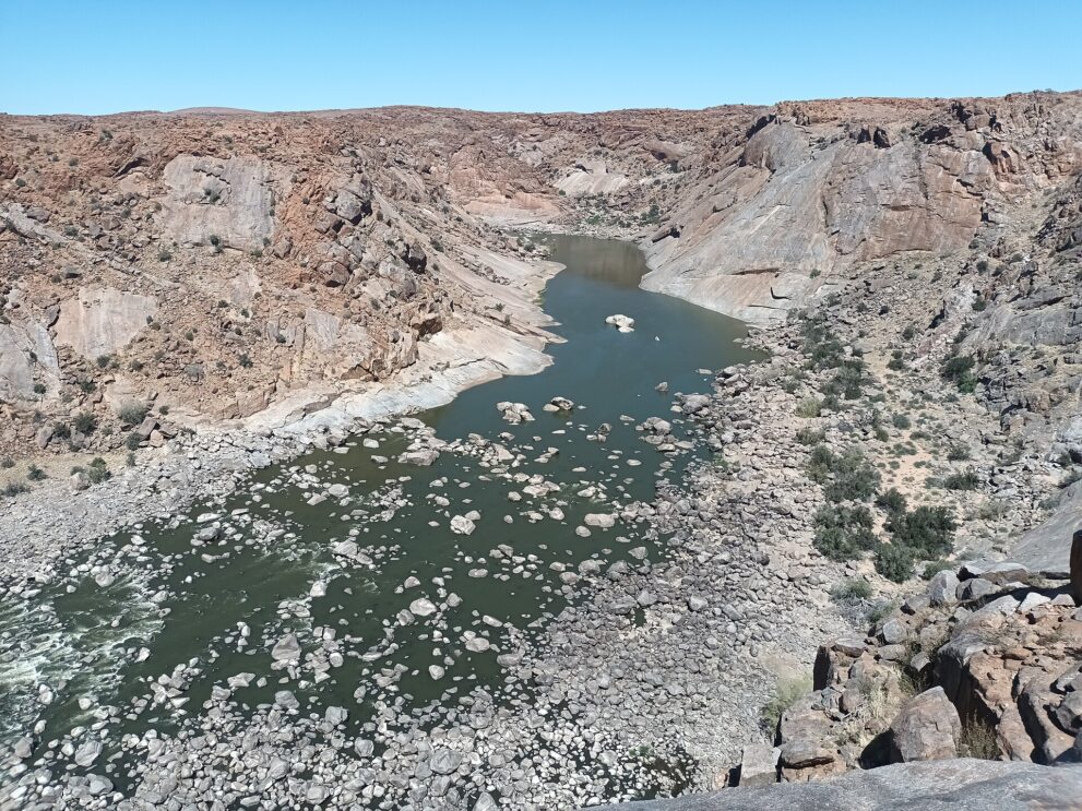 Blick von oben auf den grünen Oranje, der zwischen Geröll und hellen Granitwänden durch die Schlucht fließt.