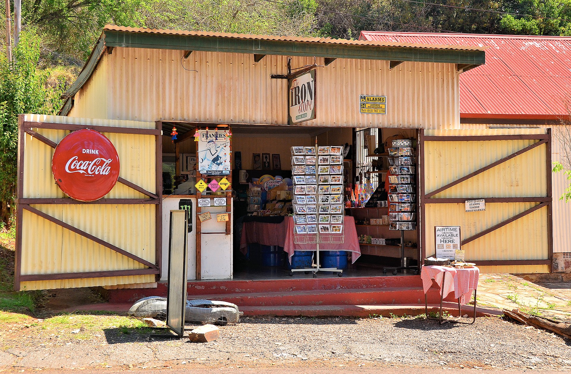 Laden aus Wellblech mit offenen Flügeltüren, Postkartenständern und einem alten Coca-Cola-Schild