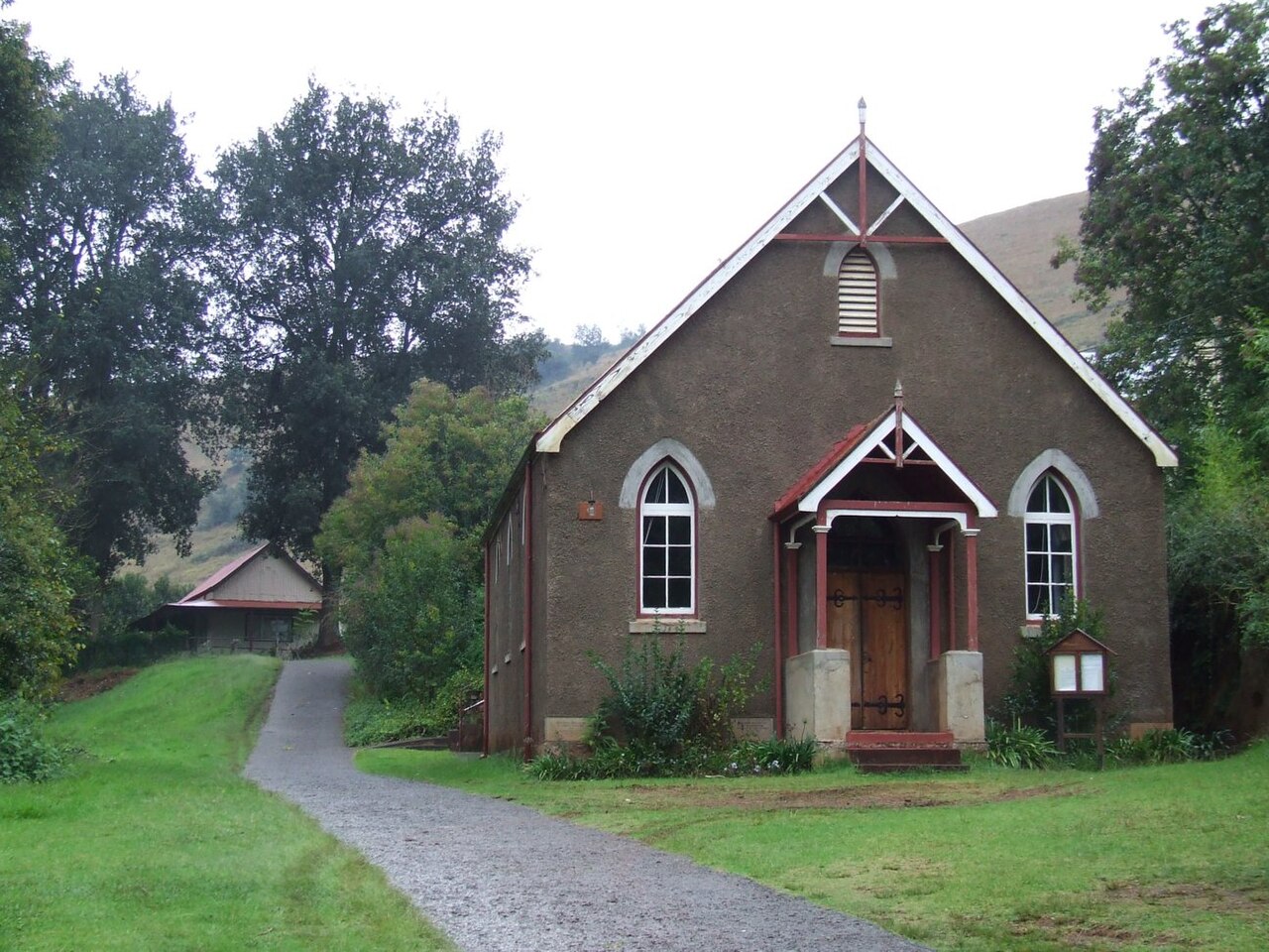 Kleine Kirche mit Spitzbogenfenstern und hölzerner Doppeltür, davor ein Kiesweg und Rasen