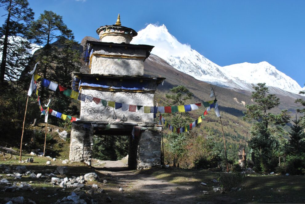 Steinernes Kani-Tor mit Gebetsfahnen am Weg von Lho nach Samagaon, dahinter der Manaslu
