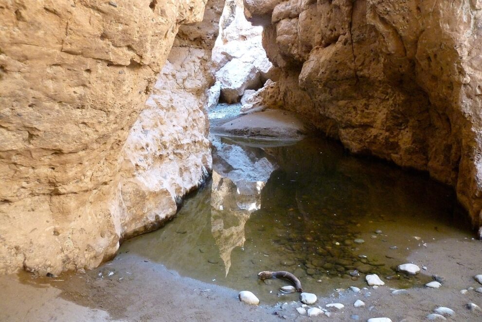 Ein stiller Tümpel am Grund der Schlucht, in dem sich die hellen Felswände spiegeln, davor runde Kiesel.