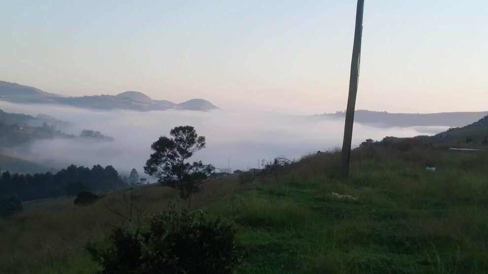 Morgennebel füllt ein Tal im Hochland von Eswatini, dahinter flache Bergkuppen im ersten Licht
