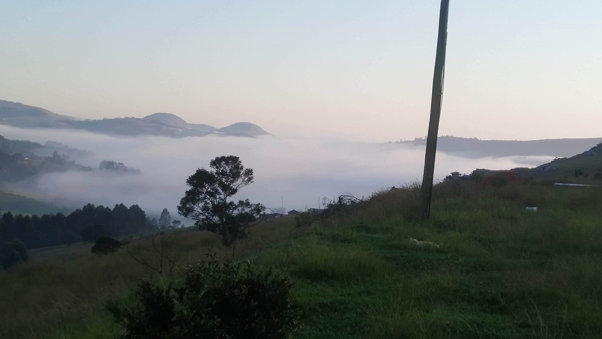 Morgennebel füllt ein Tal im Hochland von Eswatini, dahinter flache Bergkuppen im ersten Licht