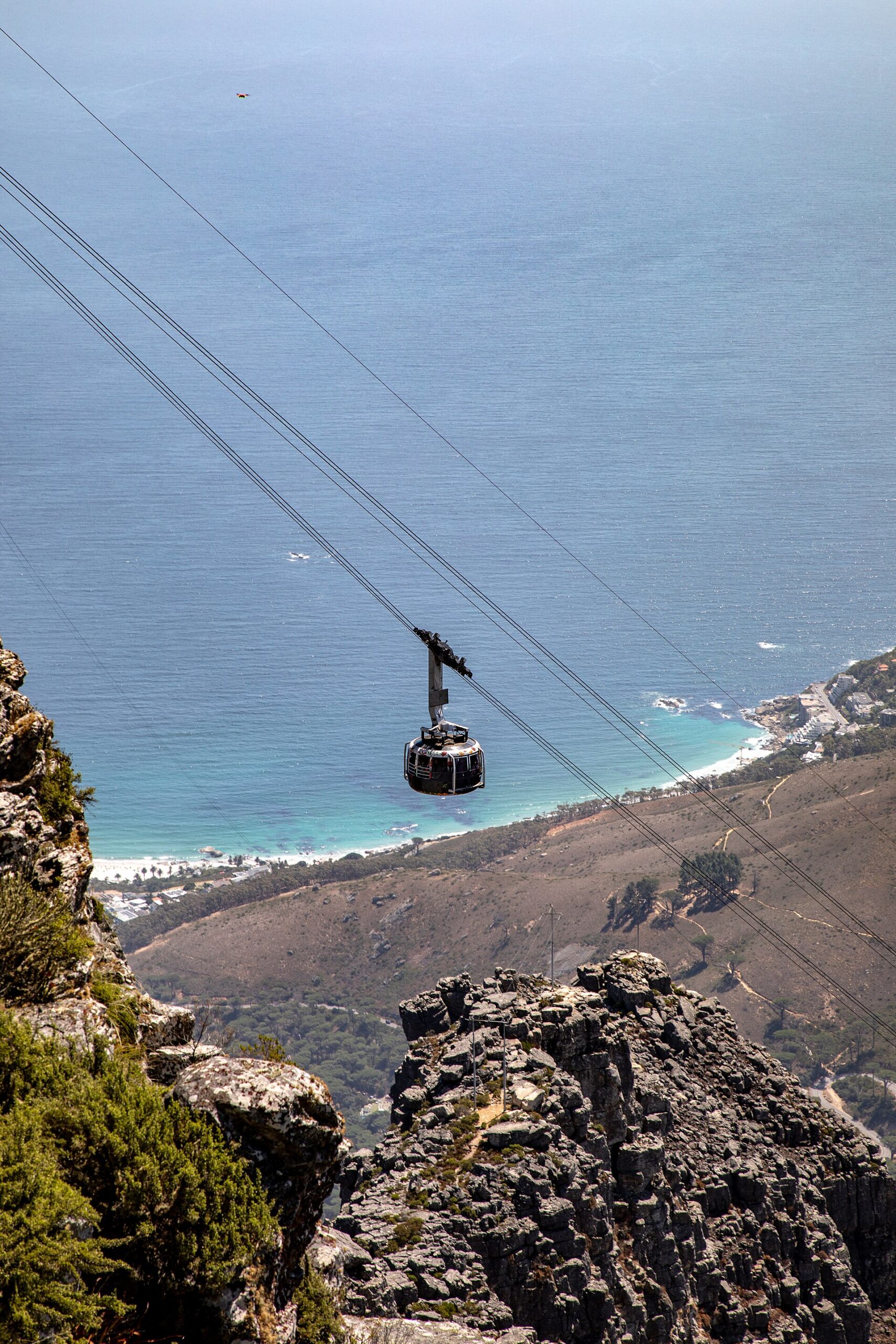 Runde Seilbahngondel an vier Tragseilen über Felsen, tief unten Strand und Häuser von Camps Bay