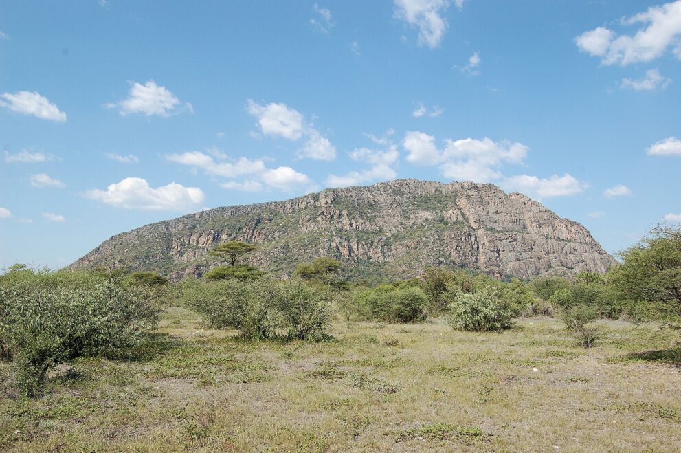 Ein langgestreckter Felshügel der Tsodilo Hills über flachem Buschland unter blauem Himmel
