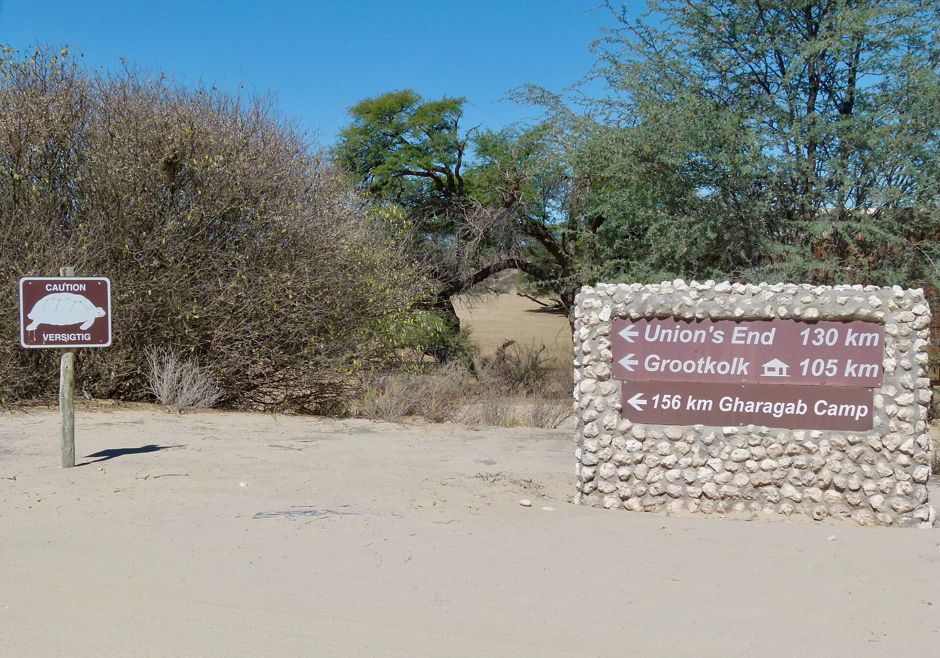 Ein gemauertes Schild aus hellen Kalksteinen an einer Sandpiste zeigt Union’s End 130 km, Grootkolk 105 km und Gharagab 156 km, links ein Schild „Vorsicht Schildkröten“