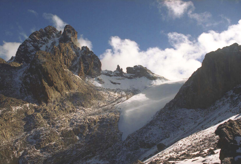 Zackige Felsgipfel mit Neuschnee, rechts zieht eine glatte weiße Gletscherzunge zwischen zwei Felsflanken herab