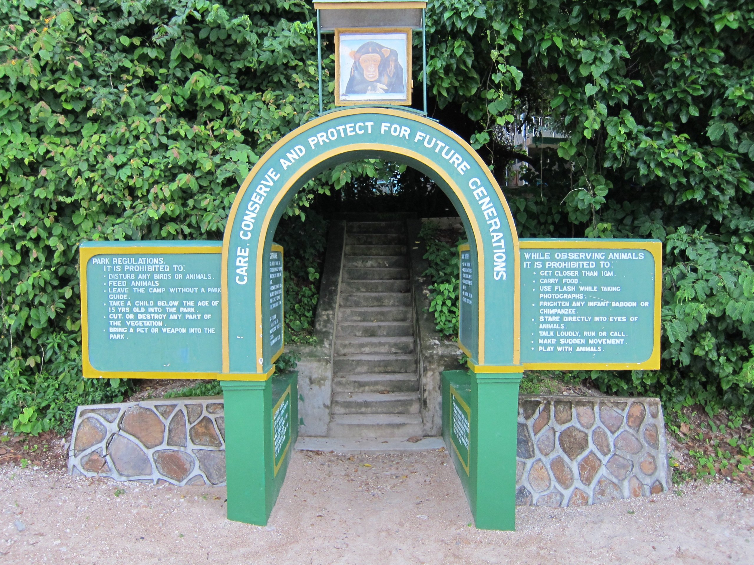 Grüner Eingangsbogen mit Tafeln zu den Parkregeln vor einer Treppe in den Wald, Gombe-Stream-Nationalpark
