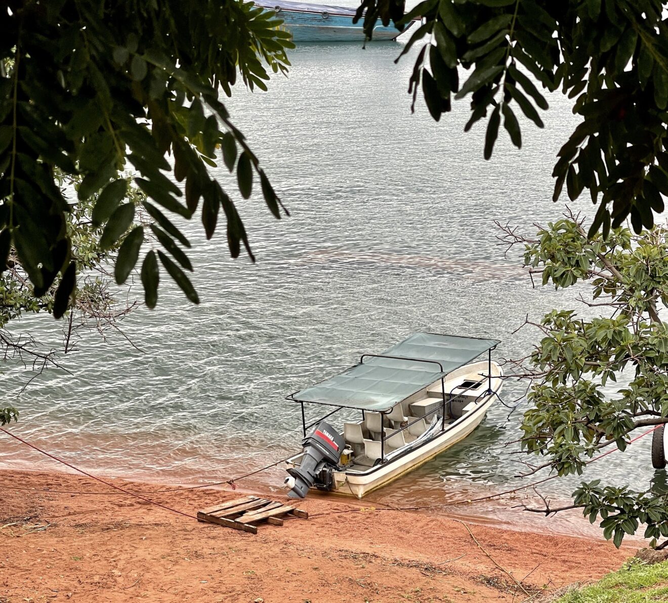 Weißes Motorboot mit Sonnendach am roten Sandufer in Kibirizi, Kigoma, am Tanganjikasee