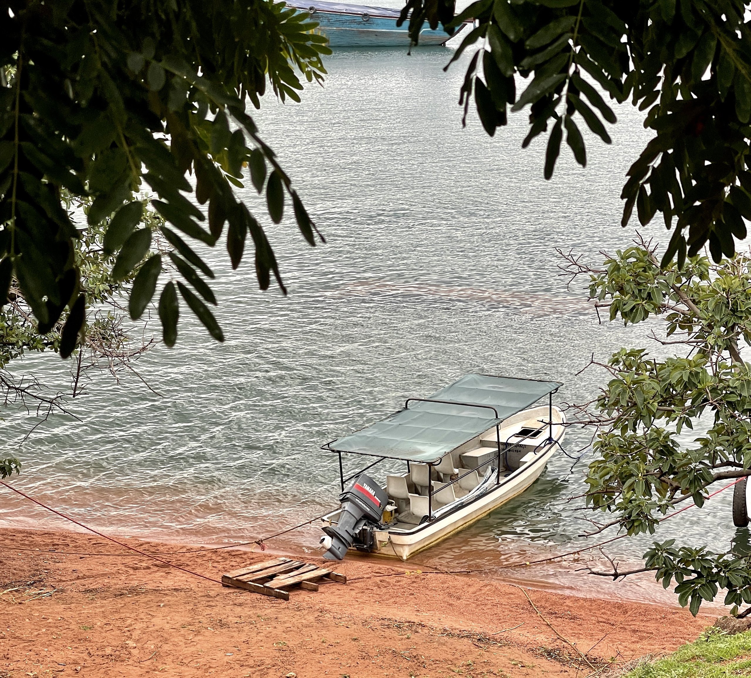 Weißes Motorboot mit Sonnendach am roten Sandufer in Kibirizi, Kigoma, am Tanganjikasee