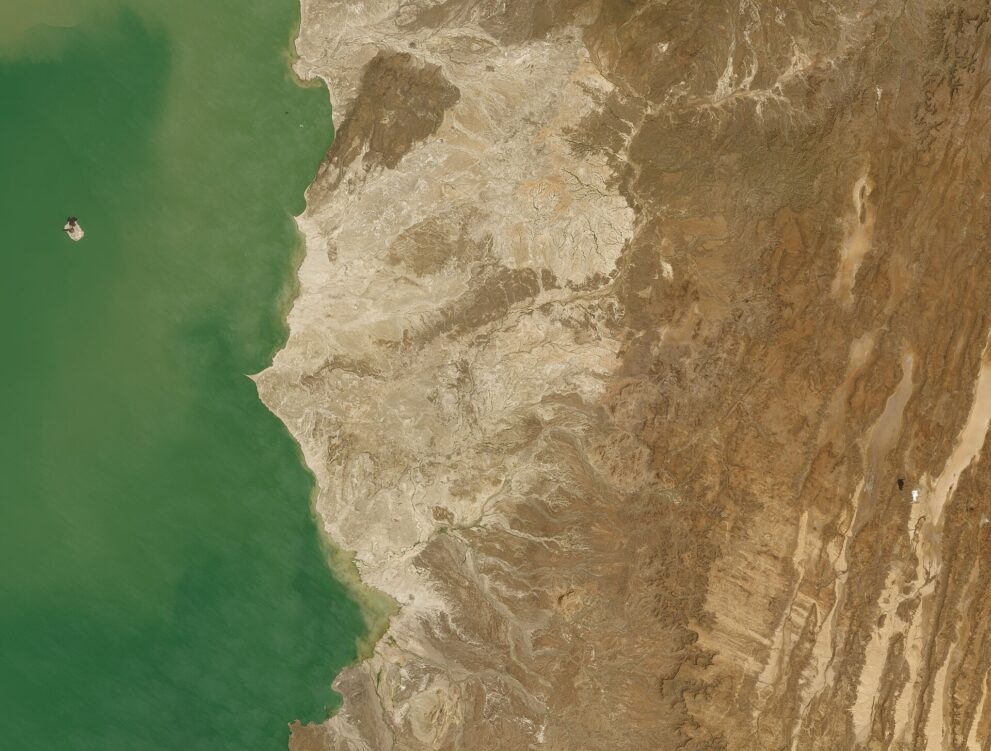 Satellitenbild: grüner See links, rechts helles, zerfurchtes Land und braune Hügel